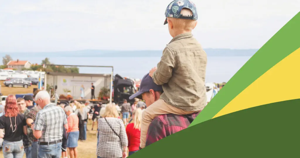 barn sitter på en persons axlar bland en folkmassa på ett evenemang en sommardag